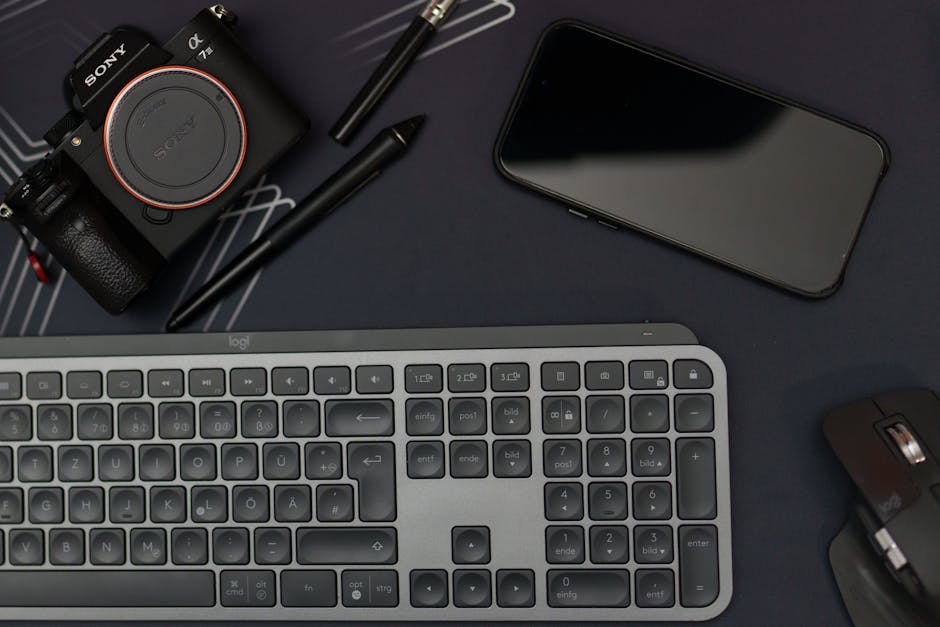 Flat lay of a modern workspace featuring a camera, smartphone, keyboard, and mouse.